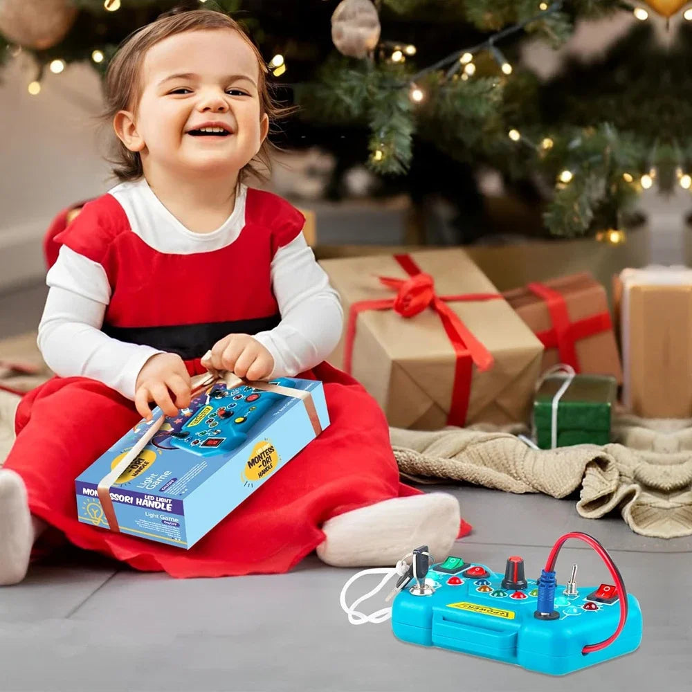 Child in a red dress playing with a toy circuit board in front of a Christmas tree and presents.